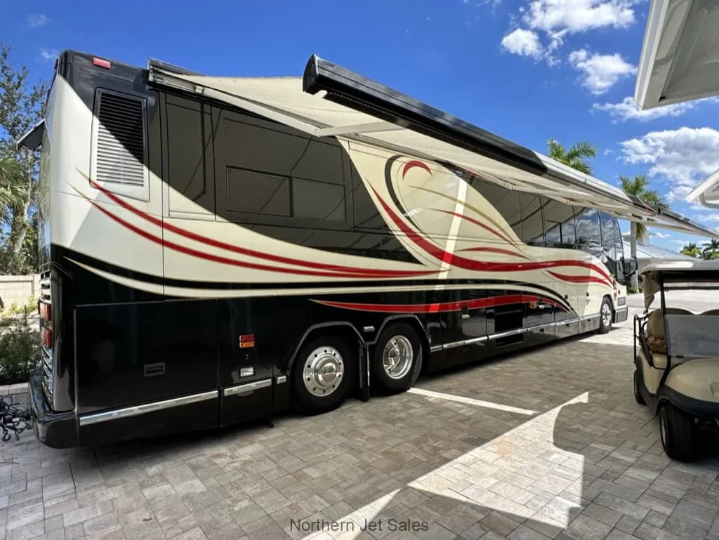 Side view of a Prevost coach with a black, white, and red paint scheme parked outside with the awning extended.