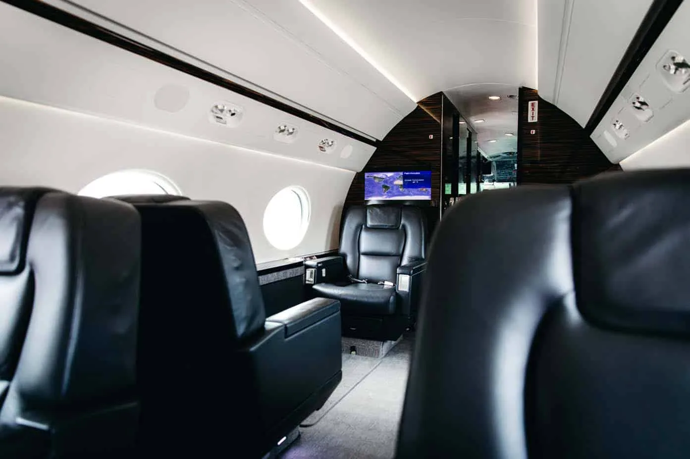A view inside the Gulfstream G550 cabin, showing black leather seats and a monitor displaying a map.