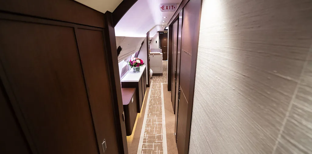 A long, luxurious aircraft hallway with dark wood paneling and an 'EXIT' sign visible at the far end.