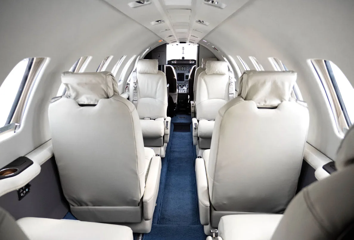 Aircraft interior with white leather seats and blue carpet, looking towards the cockpit.