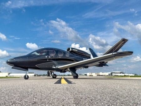 A black Cirrus Vision Jet sits on the runway under a blue sky.