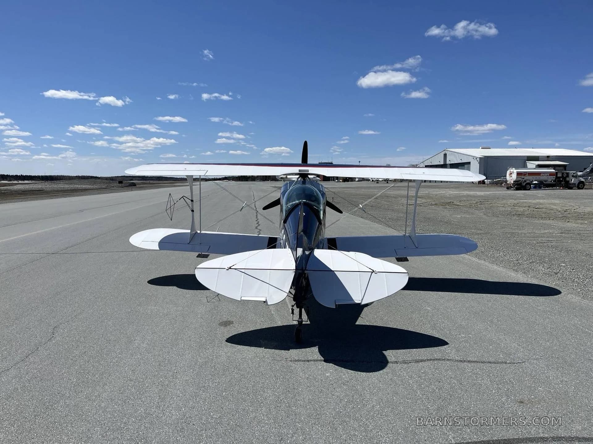 A rear view of the dark blue and white biplane C-GOJF parked on an airfield under a bright blue sky.