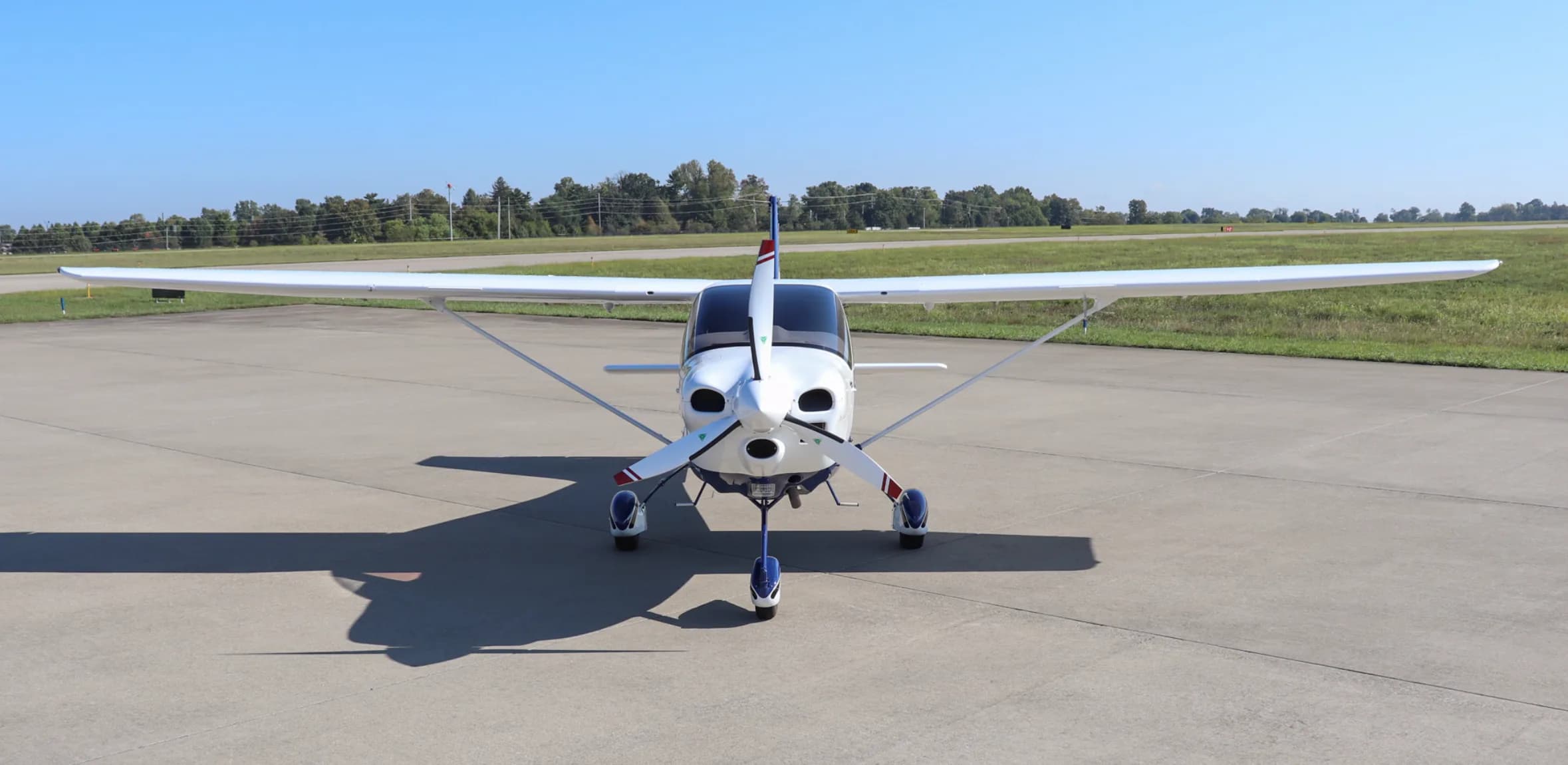 A head-on view of the white and blue Tecnam P2010 aircraft, registration N127PM, parked on an airfield.