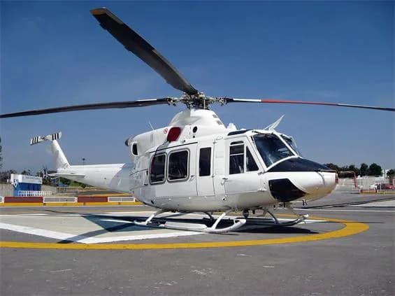 A white Bell 412 helicopter with a black nose is parked on a helipad under a clear blue sky.