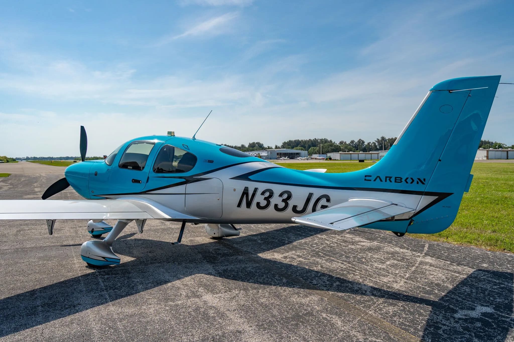 A three-quarter rear view of a blue and silver Carbon aircraft (N33JG) parked on an asphalt ramp.