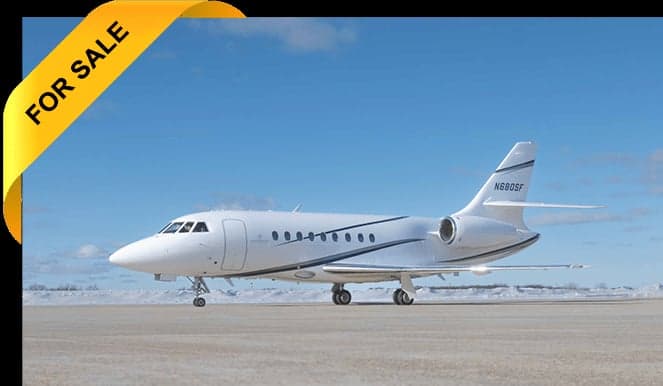 A white jet with blue and gray stripes is parked on the tarmac with a 'FOR SALE' banner.