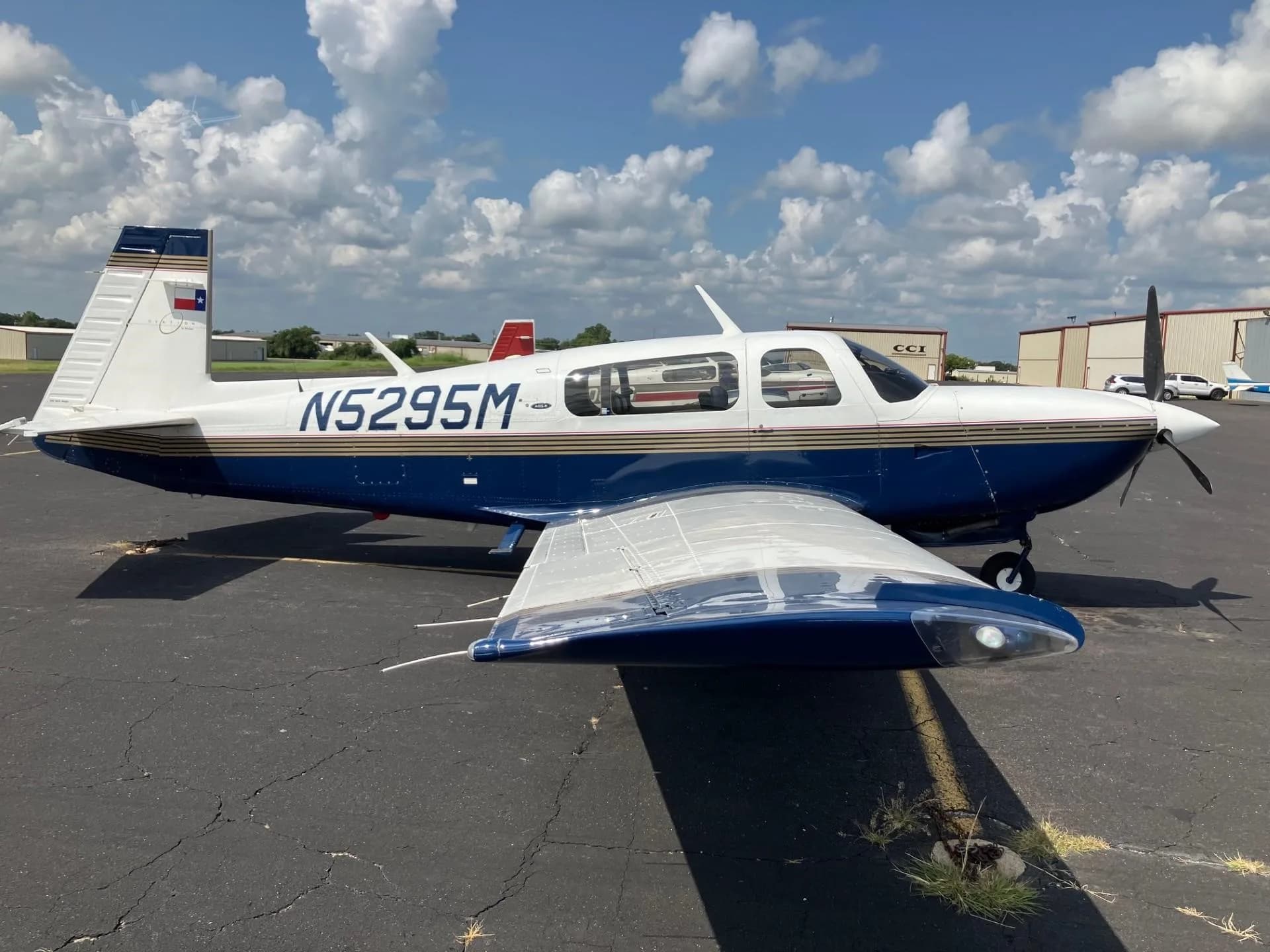 A blue and white single-engine aircraft with registration N5295M and a Texas flag on its tail, parked on an airport tarmac.