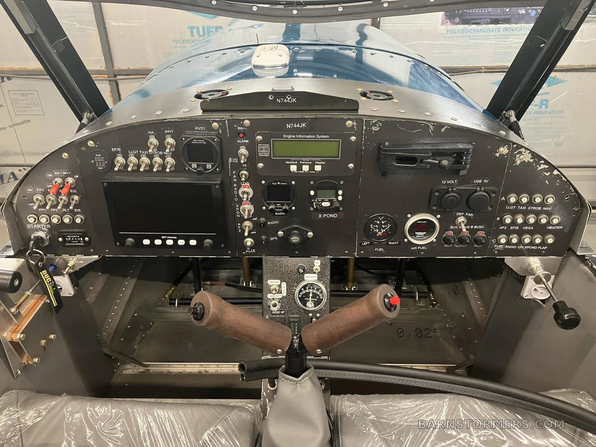A straight-on view of the Zenith CH650 cockpit, featuring a black instrument panel with dual wooden control sticks and various avionics.