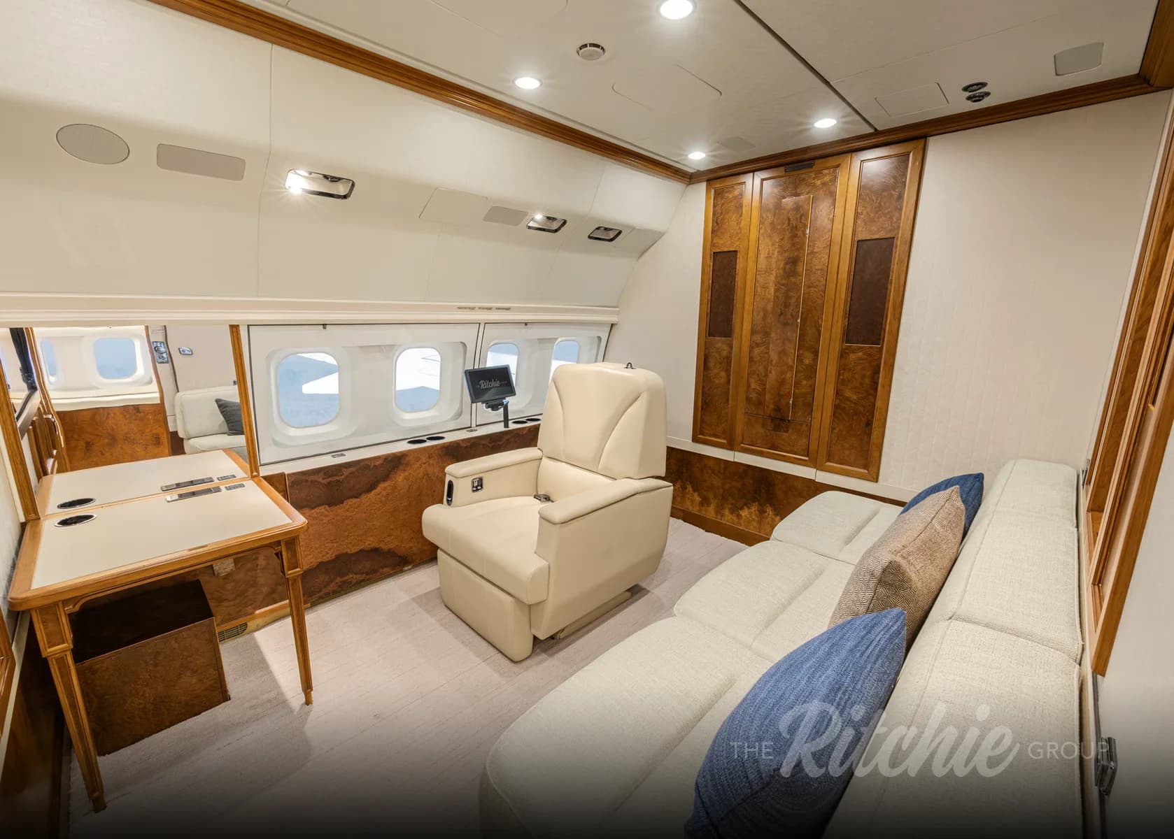 A private section of an aircraft cabin featuring a light-colored sofa, a recliner, and a desk with a window view.