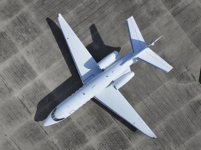An overhead view of a white business jet parked on a concrete apron, casting long shadows.