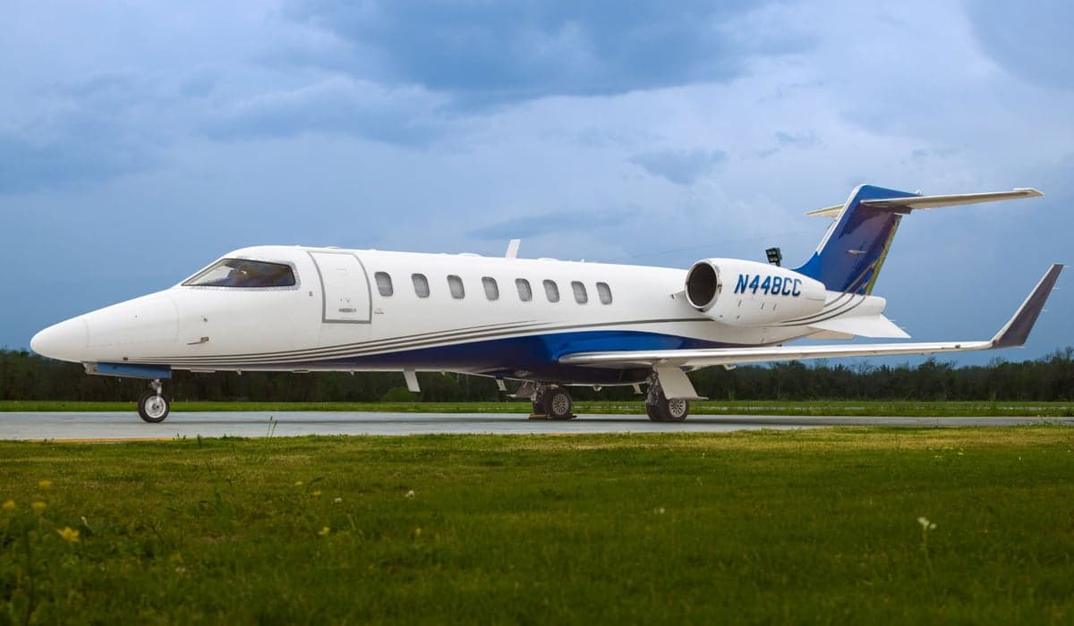 A white and blue Learjet sits on the tarmac on a cloudy day.
