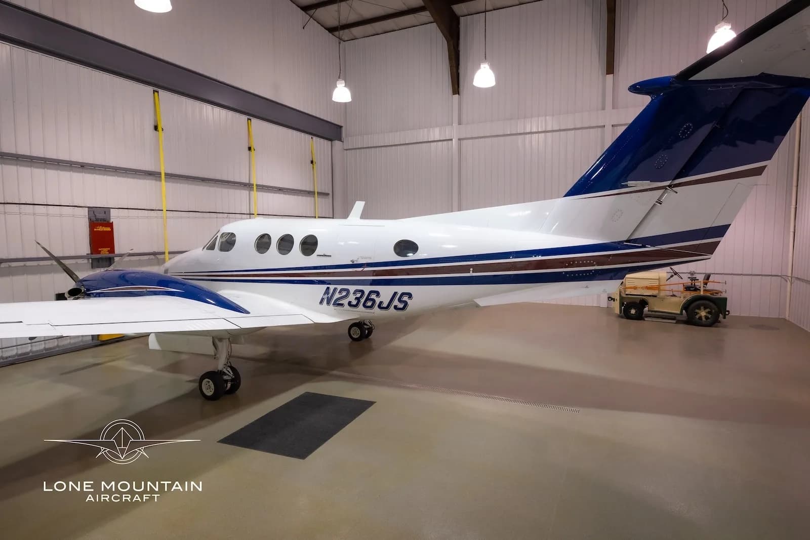 A white and blue twin-engine turboprop aircraft, N236JS, is viewed from the rear-right in a hangar.