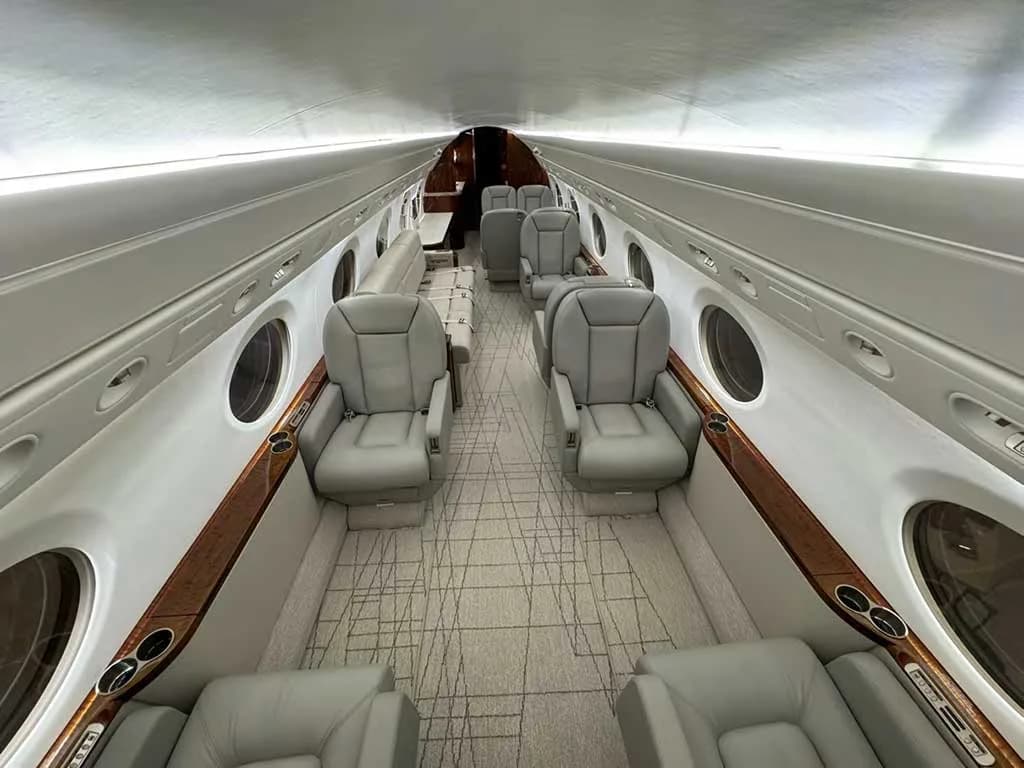 A perspective view down the aircraft cabin, highlighting light gray leather seats and a patterned aisle carpet.