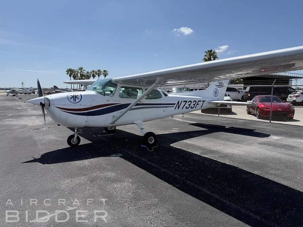 A white Cessna Skyhawk N733FT with blue and red stripes parked on an asphalt ramp under a clear sky.