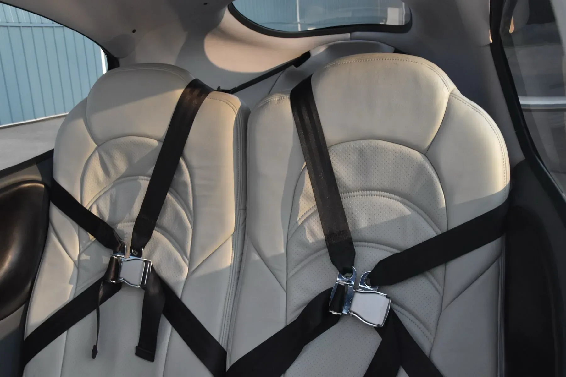 Two light-colored leather rear passenger seats with black seatbelts inside the aircraft cabin.