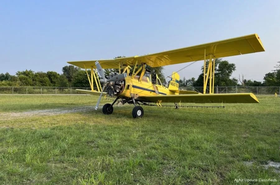 A yellow biplane crop duster, registration N66750, parked on a grassy field under a clear sky.