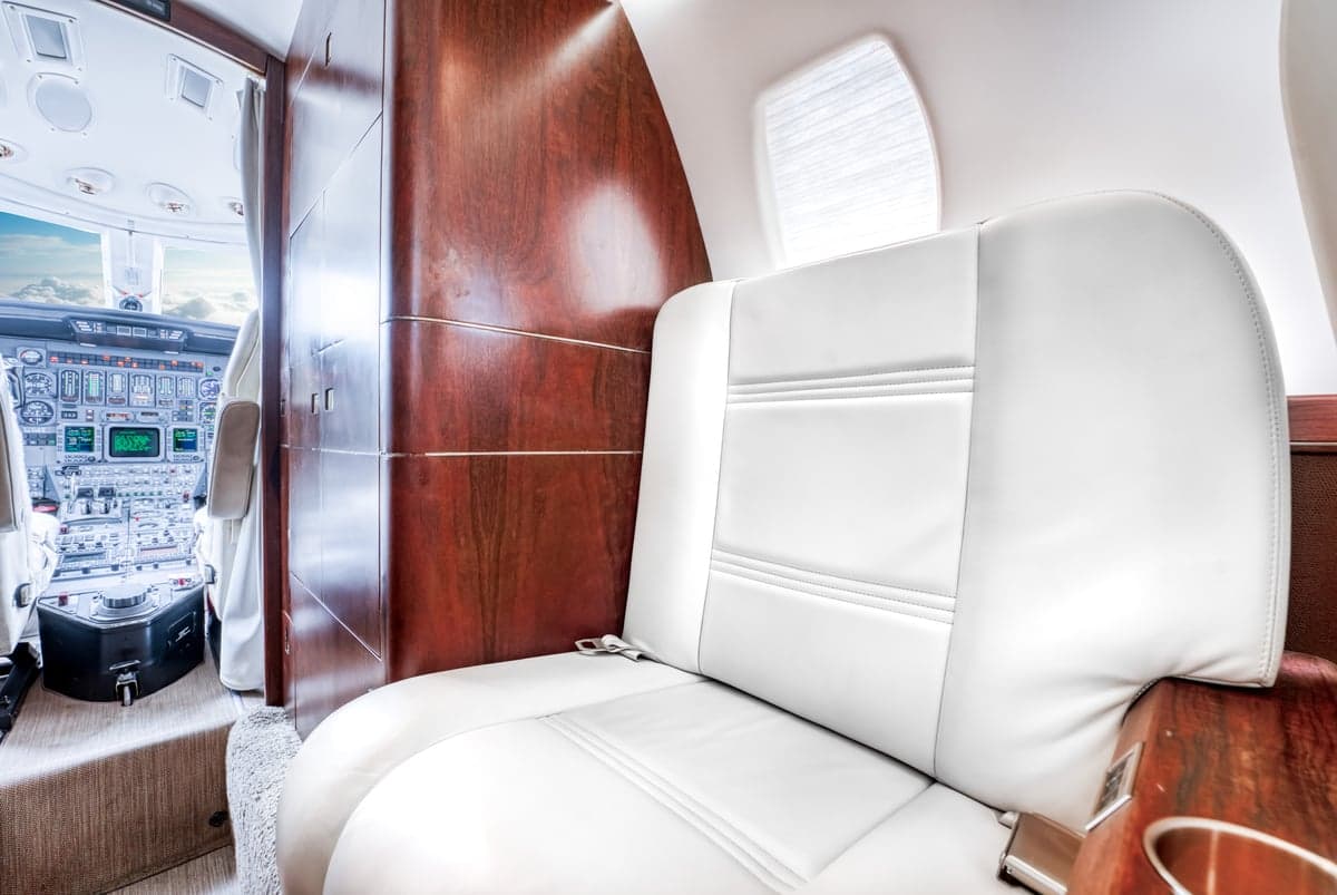 View of the interior cabin of a Cessna Citation CJ3+ with a white leather seat and cockpit in the background.