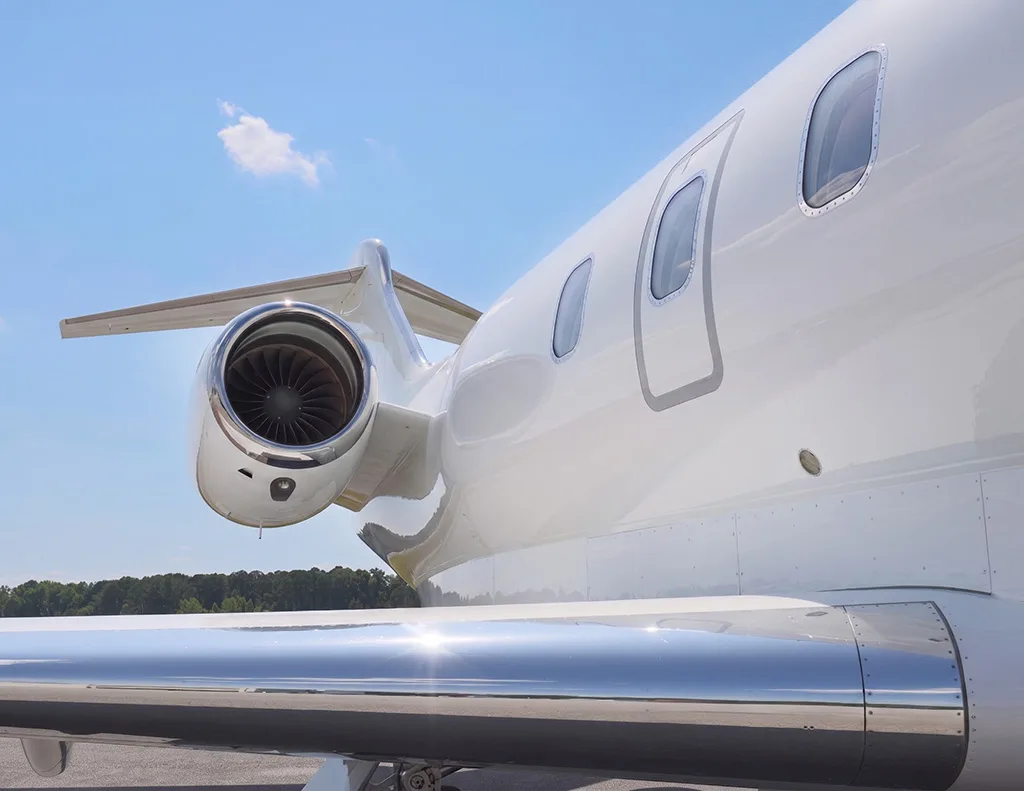 A close-up view of the rear fuselage, engine, and wing of a white business jet under a blue sky.