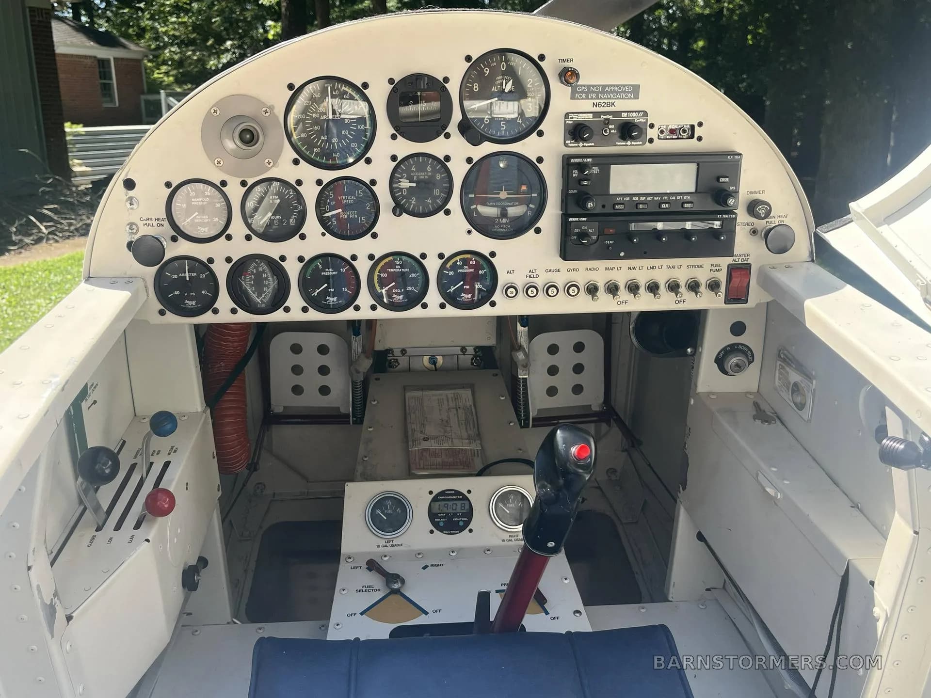 The cockpit of a small aircraft, showing a white instrument panel with various gauges, radios, and flight controls.