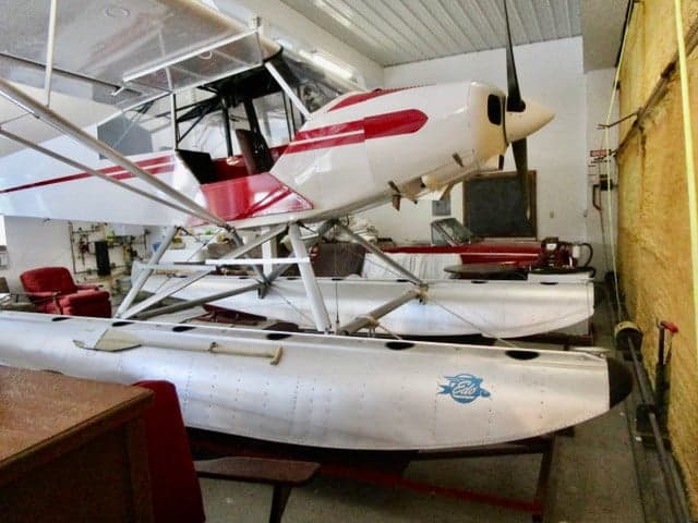 A white and red float plane is parked inside a hangar.