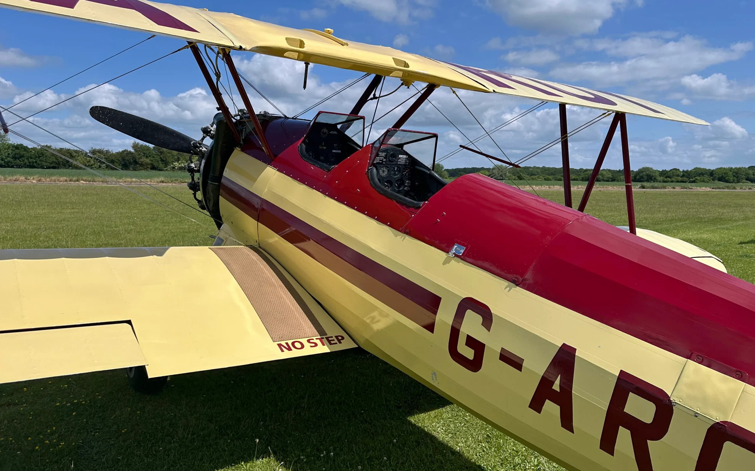 A side view of the yellow and red Stearman biplane's fuselage, showing the cockpit and "NO STEP" marking on the wing.