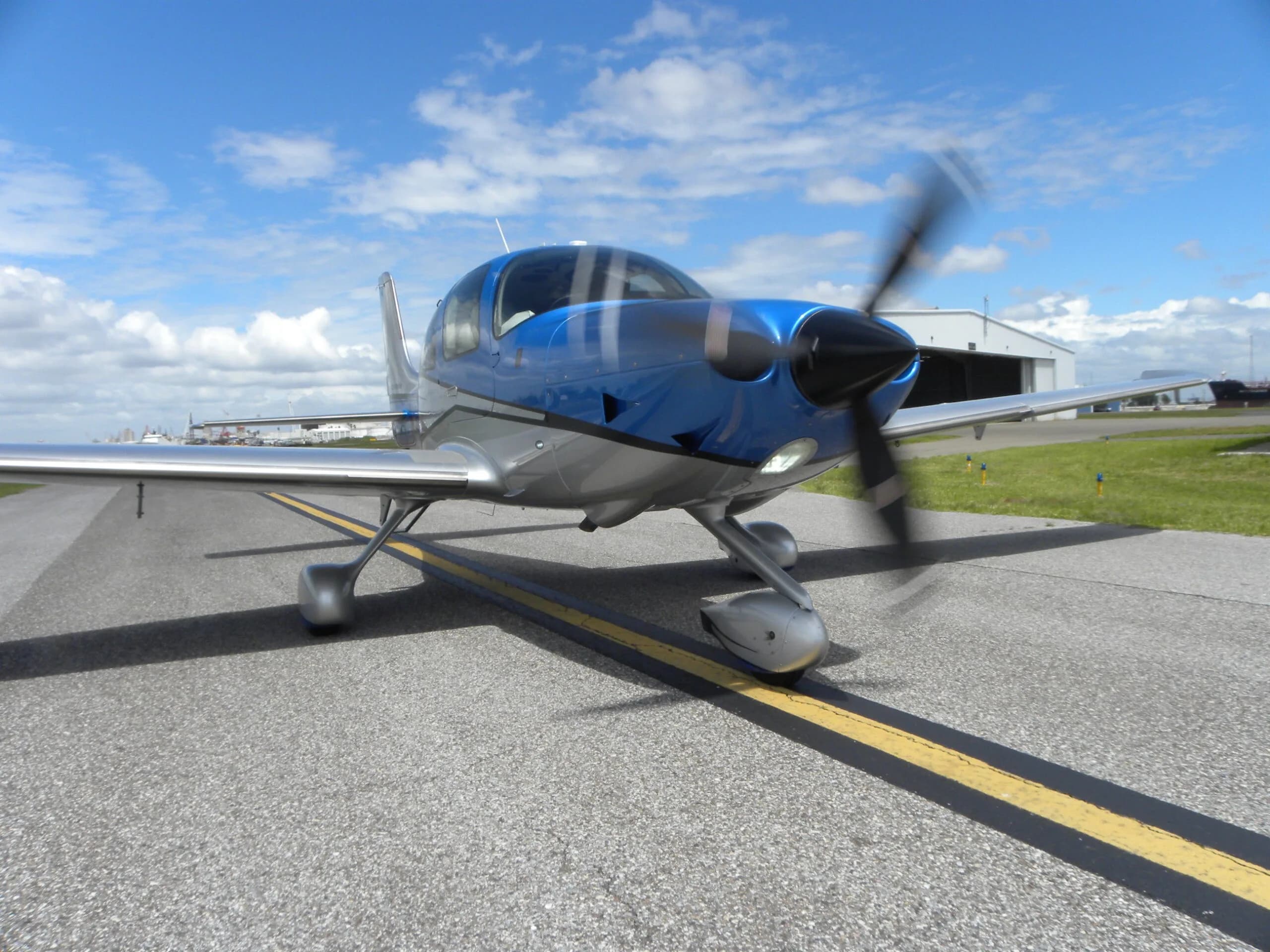 A front-side view of a blue and silver Cirrus SR22T aircraft, N313JB, with its propeller spinning on a taxiway.
