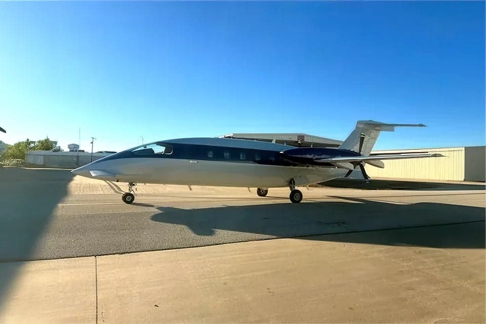 A Piaggio Avanti EVO aircraft is parked on the tarmac with a blue and white paint scheme.