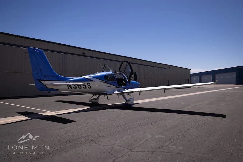 A rear three-quarter view of the blue and silver Cirrus SR22 aircraft, N365S, with its doors open, parked on an asphalt ramp.