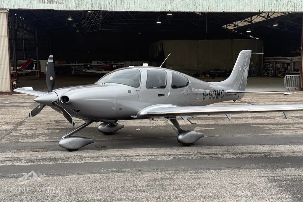 A front-side view of the silver Cirrus SR22 aircraft with its doors closed, parked on an airfield.