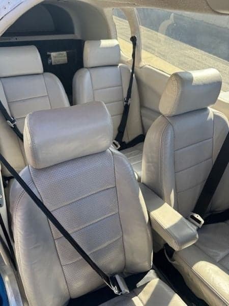 View of the aircraft's four light-colored leather seats with black seatbelts.