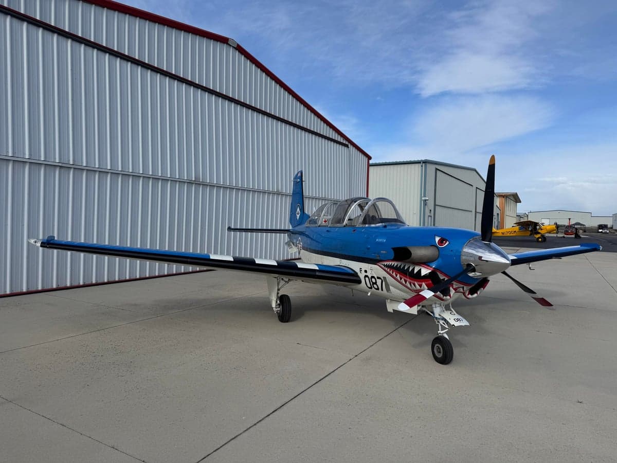 A blue and white SIAI-Marchetti SF.260 is parked on the tarmac with a shark mouth paint scheme.