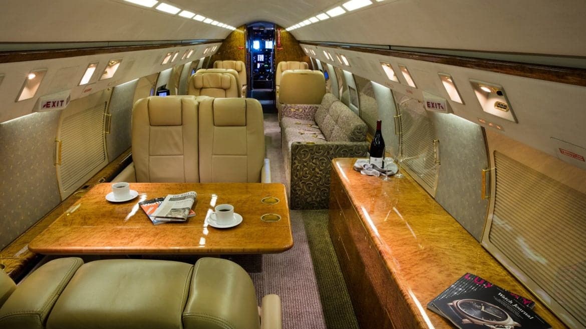 Spacious interior of the aircraft with leather seating, wooden tables, and a sofa.