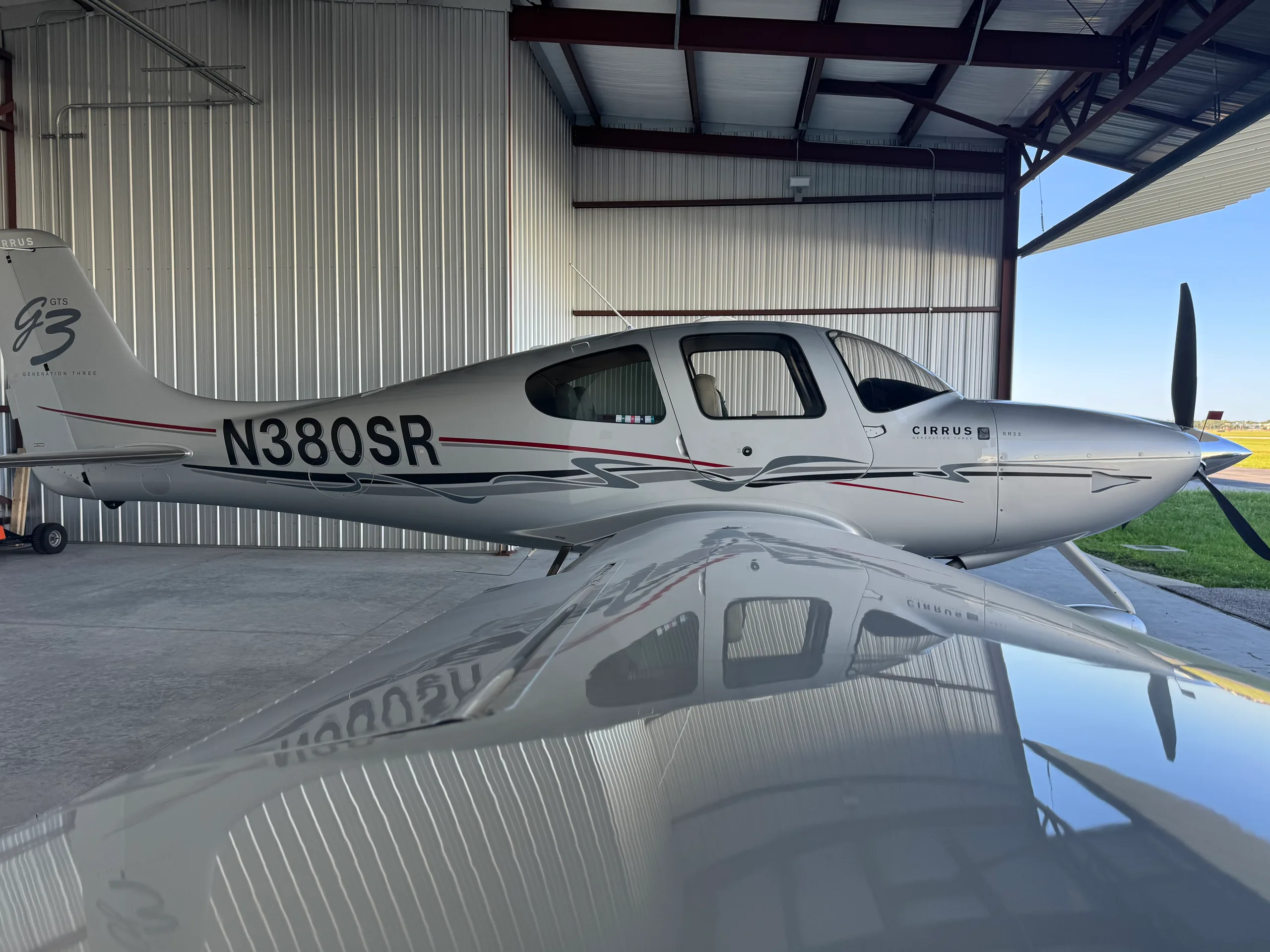 A silver Cirrus SR22 Generation Three aircraft with N380SR registration is parked in a hangar, viewed from the right side.