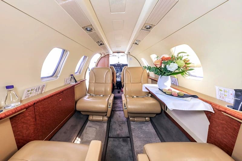 Aircraft cabin with tan leather seats and a table with flowers.