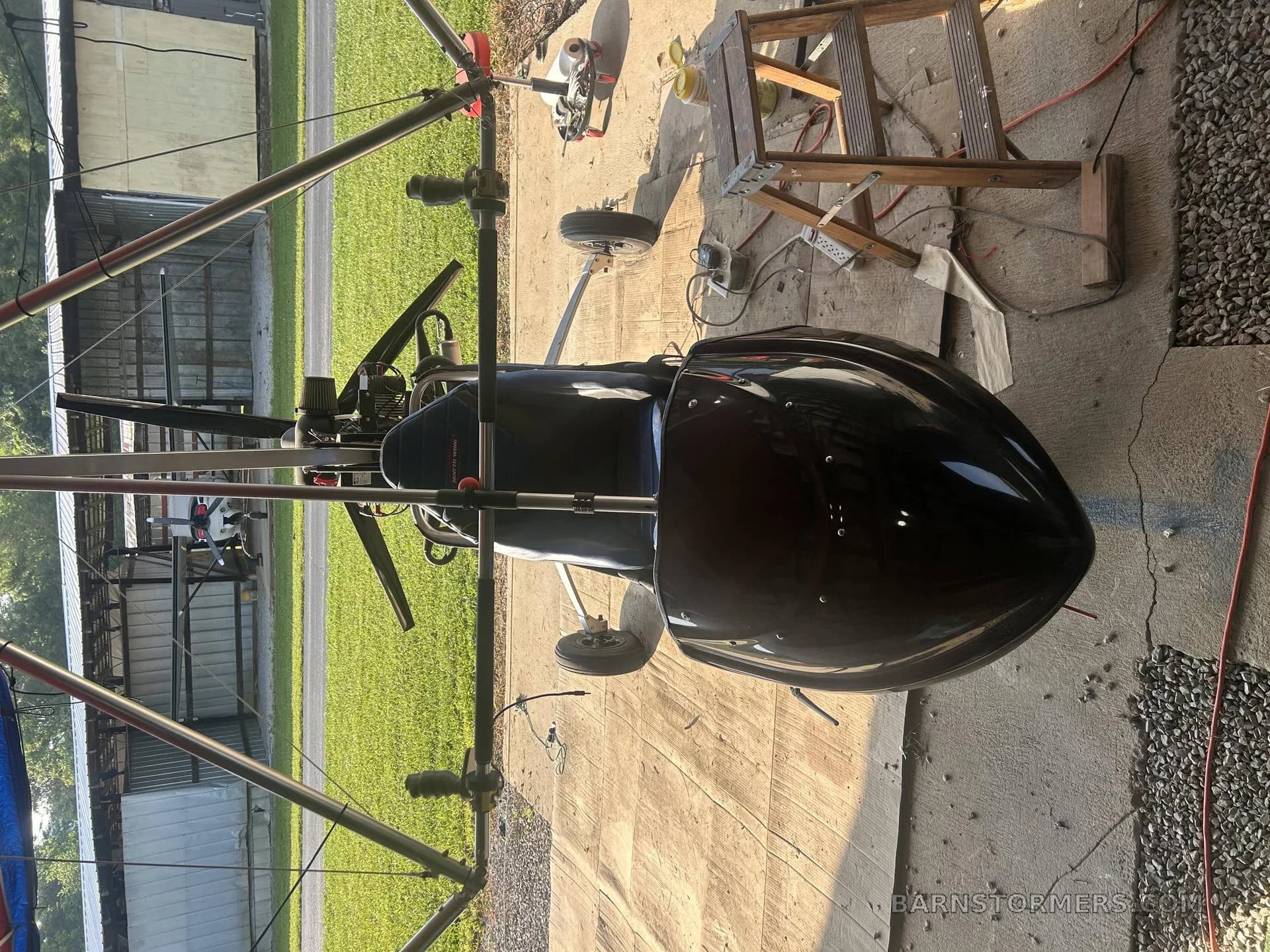 A black ultralight autogyro with a single seat and exposed frame, parked on a concrete pad.