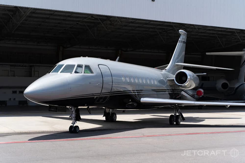 A silver and black business jet parked on an airport tarmac, viewed from the front-right.