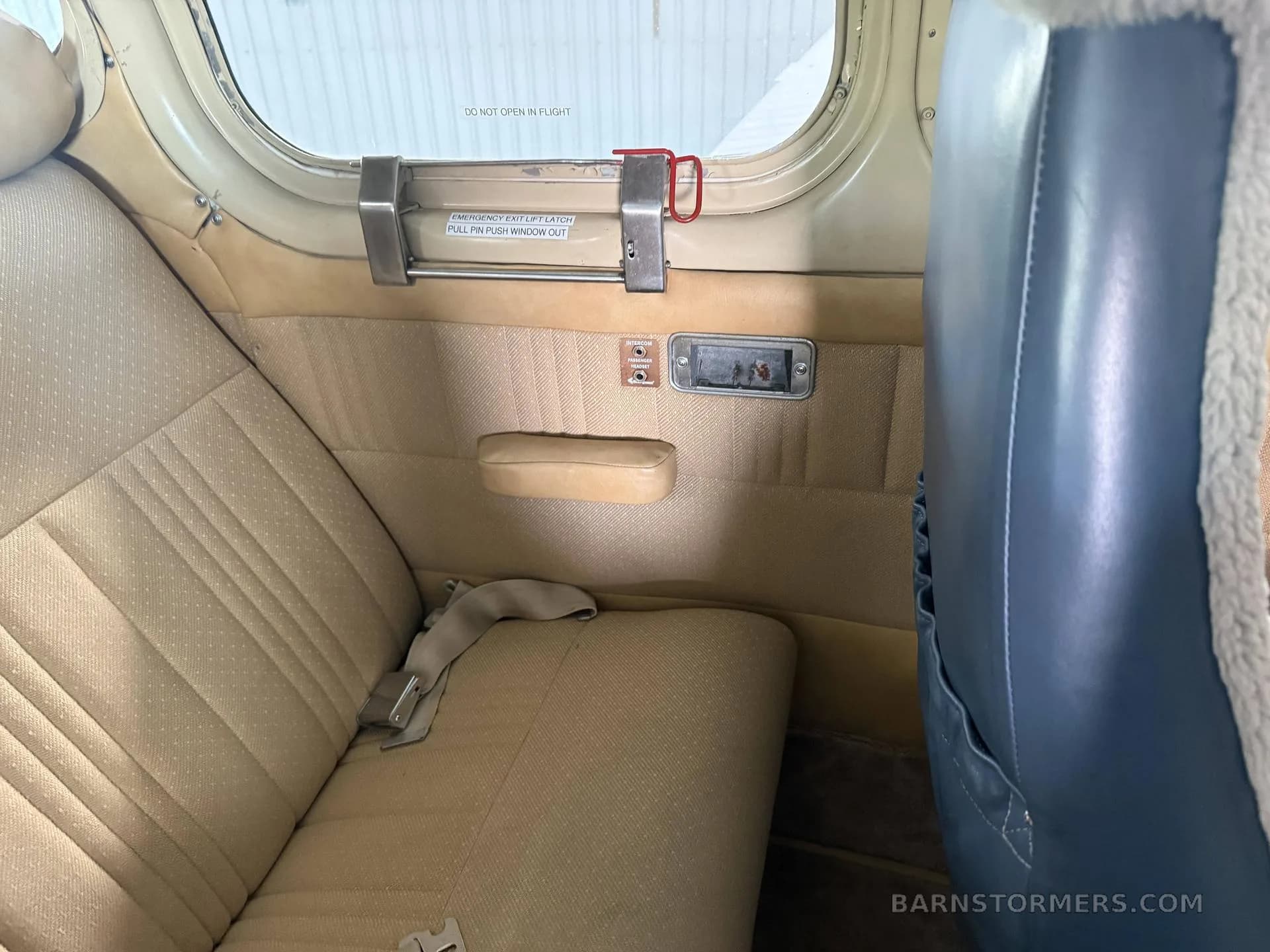 The beige rear cabin seats and window of a small aircraft, showing an emergency exit latch.