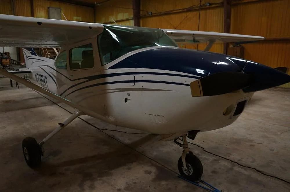 A white and blue Cessna 182 Skylane N735HT is parked in a hangar, viewed from the front.