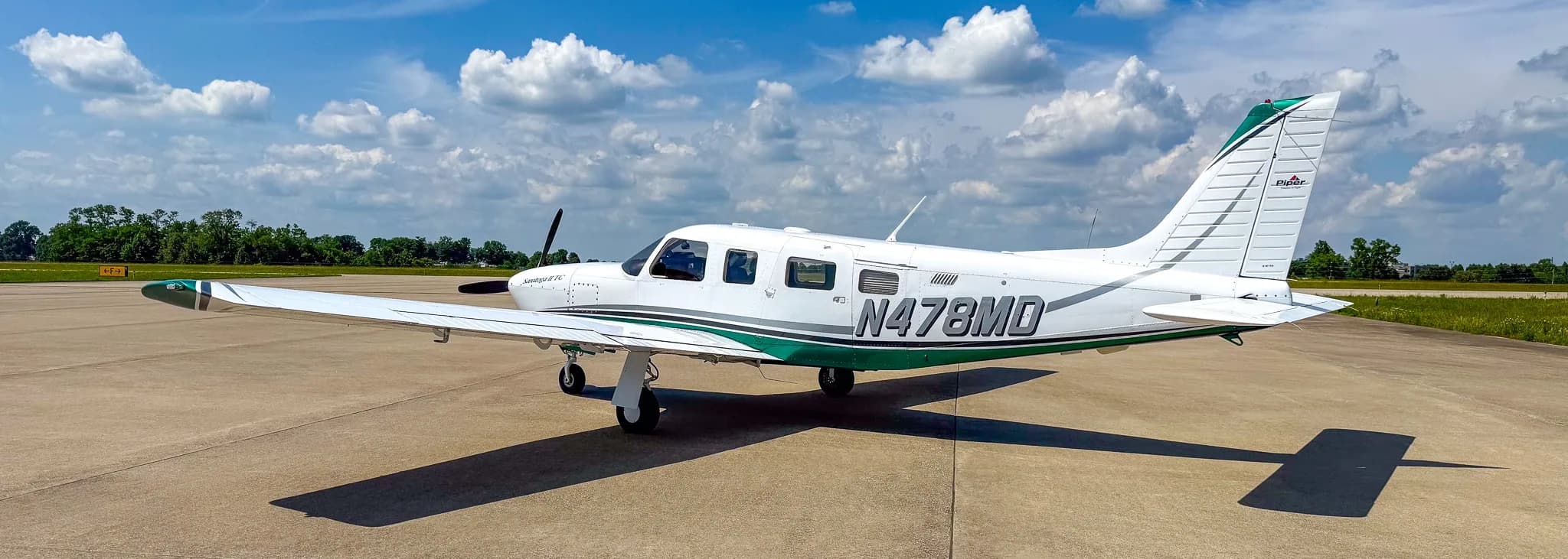 A side view of the white and green Piper Saratoga II TC aircraft (N478MD) with its tail visible, parked on an airfield.