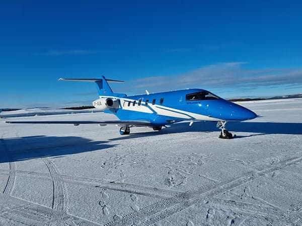 A blue and white Pilatus PC-24 on a snowy airfield.