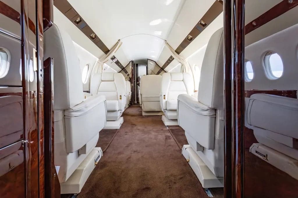 A view down the aisle of the aircraft cabin with white leather seats.