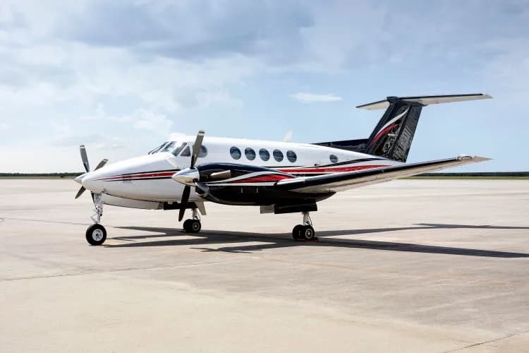 A white and black twin-turboprop aircraft with red stripes is parked on an airfield under a partly cloudy sky.