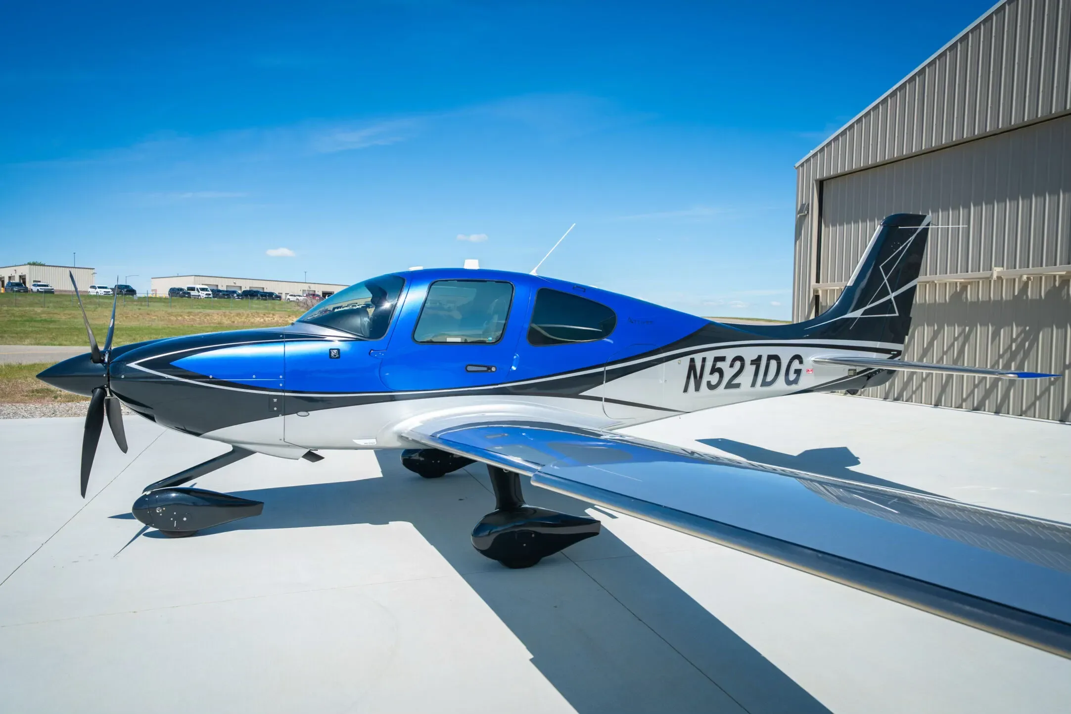 A three-quarter front view of the blue, black, and white Cirrus SR22T aircraft N521DG, highlighting its polished wing.