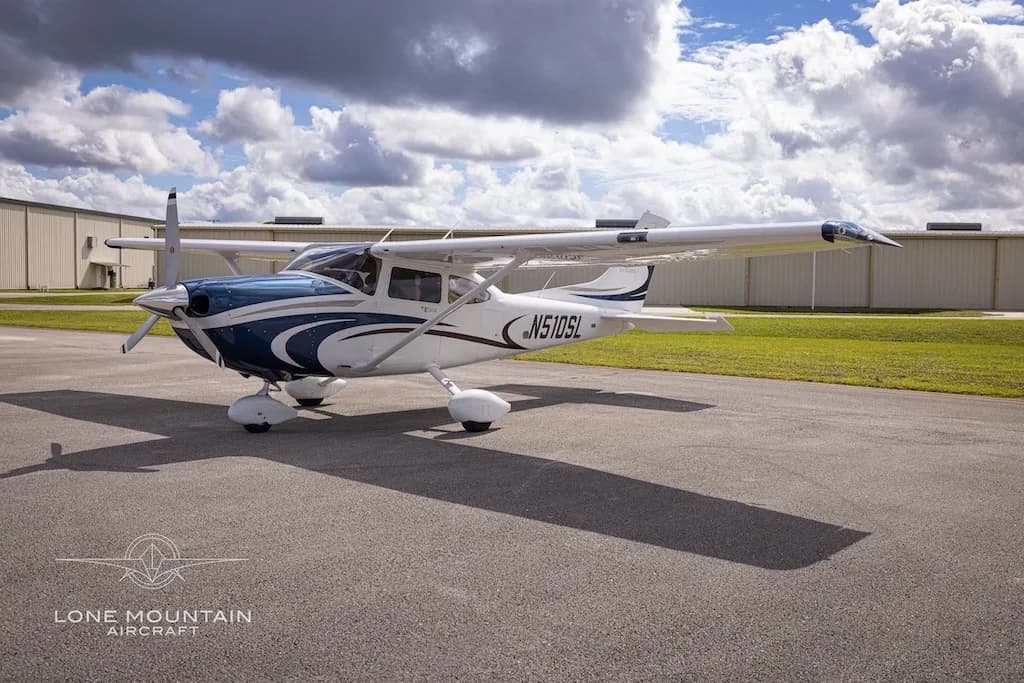 A white and blue Cessna 182 Skylane aircraft, N510SL, is parked on an airfield under a partly cloudy sky.
