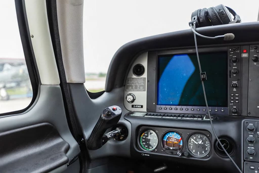A close-up view of the right side of an aircraft cockpit, showing a display screen, analog gauges, and a side yoke.