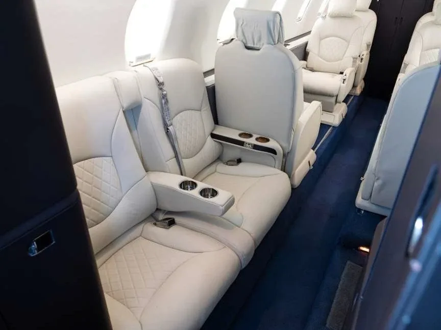 A close-up view of the light beige leather seats in the business jet cabin, featuring diamond stitching and cup holders.