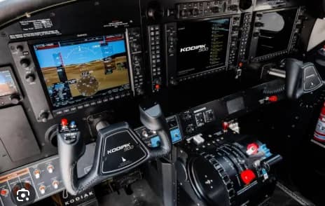 The cockpit of a Kodiak 100 aircraft with multiple Garmin displays and flight controls.