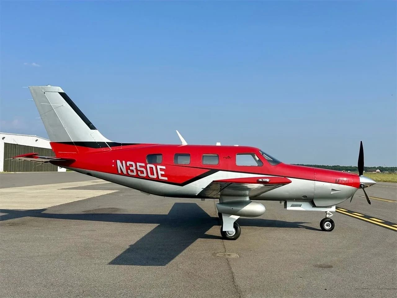 A side view of the red and silver Piper M350 aircraft, registration N350E, parked on an airport tarmac.