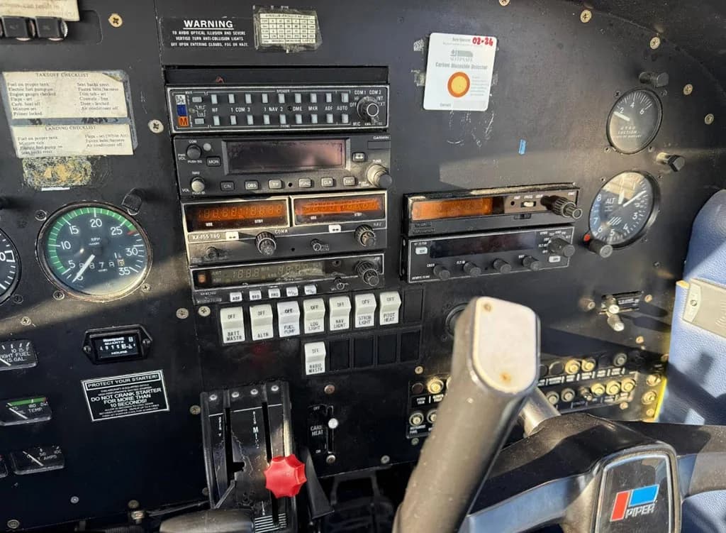 A close-up view of the center instrument stack in a small aircraft cockpit, showing radios, switches, and engine control levers.