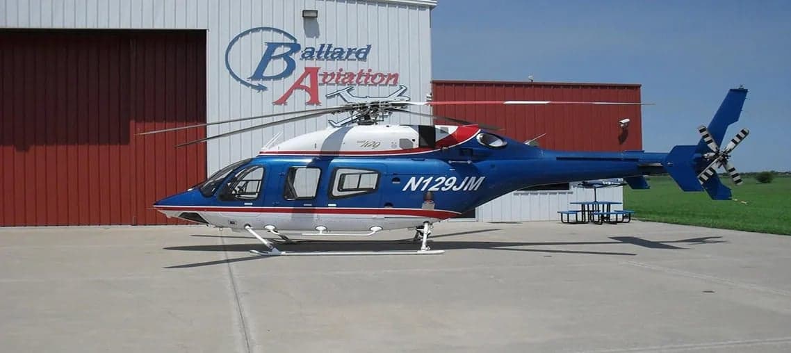 A blue and white Agusta 109 helicopter is parked in front of a hangar.
